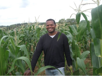 A photo of David Mwanaka, smiling in a crop field of white maize